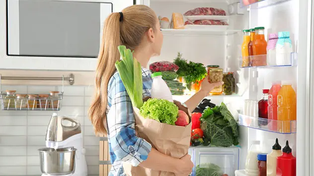 Frau räumt frische Lebensmittel in den Kühlschrank ein