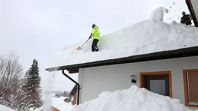 Männer schippen Schnee von einem Hausdach