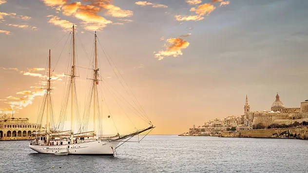 Segelboot vor der historischen Küste von Valletta auf Malta bei Sonnenuntergang, mit Blick auf die Altstadt
