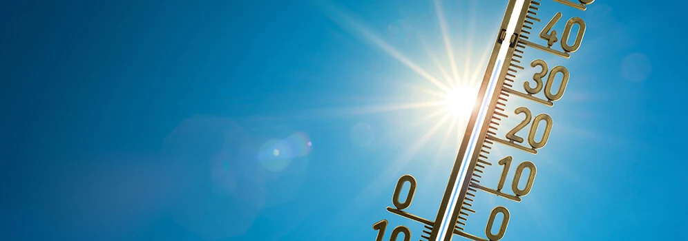 Thermometer zeigt Temperaturen über 30 Grad Celsius vor blauem Himmel mit Sonne an