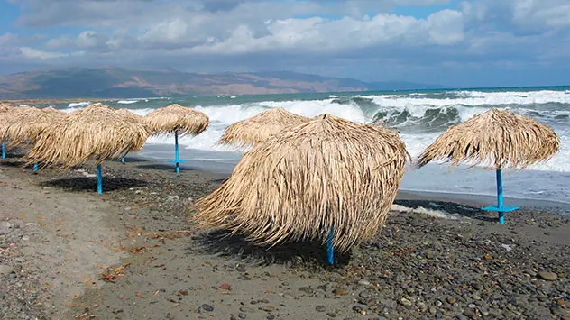 Aufgewühltes Meer und viele Wolken an einem Strand mit Sonnenschirmen in Griechenland 