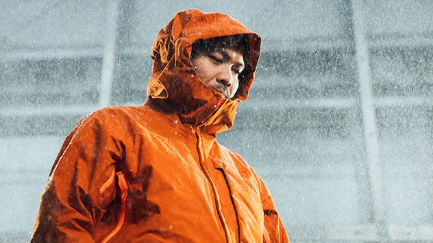 Junger Mann in orangefarbener GORE-TEX Jacke bei starkem Regen.