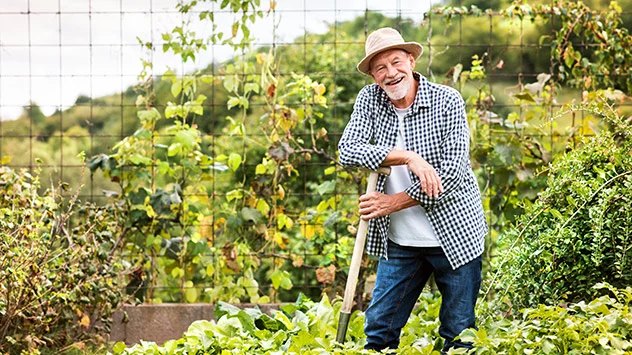 Ein Mann stützt sich bei der Gartenarbeit auf einer Schaufel ab.