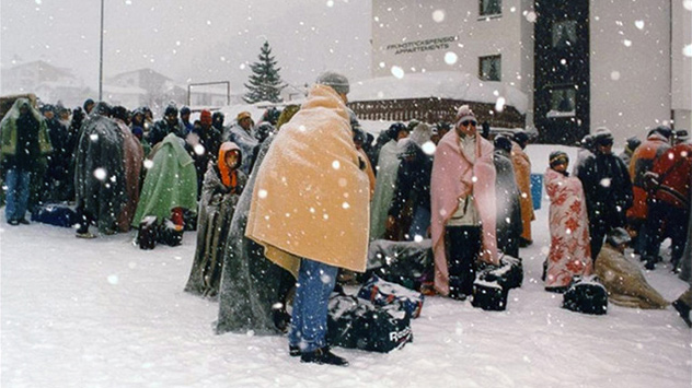 mennesker står i sne med tæpper og tasker