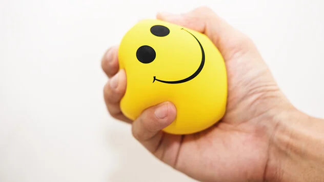 Gelber Entspannungsball mit einem Smiley-Aufdruck wird zusammengedrückt