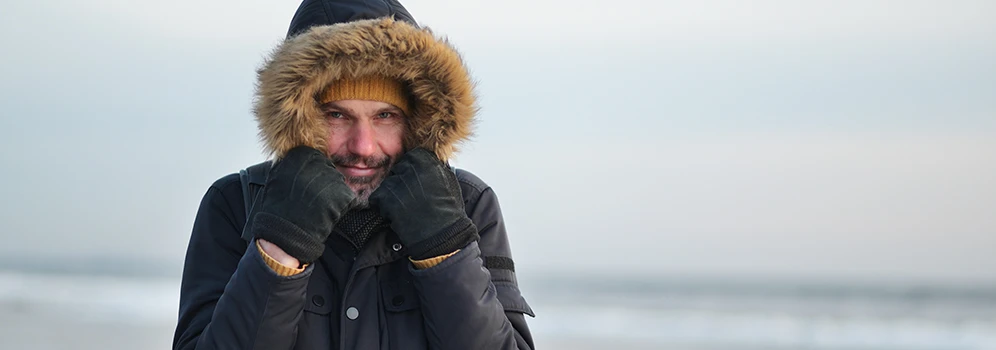 Mann am Strand mit dicker Kapuze und Handschuhen