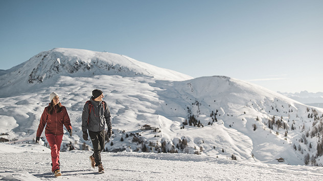 Ein Paar wandert durch die verschneite Landschaft, im Hintergrund Berge.