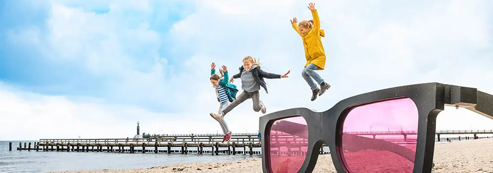 Kinder springen am Strand von Zingst über eine große Sonnenbrille