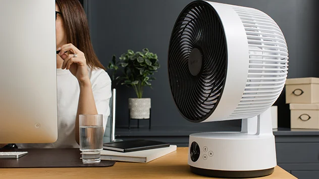 Eine Frau arbeitet am Schreibtisch, auf dem ein Meaco-Ventilator steht. 