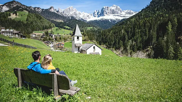 Paar sitzt auf einer Bank und blickt auf das Alpenpanorama