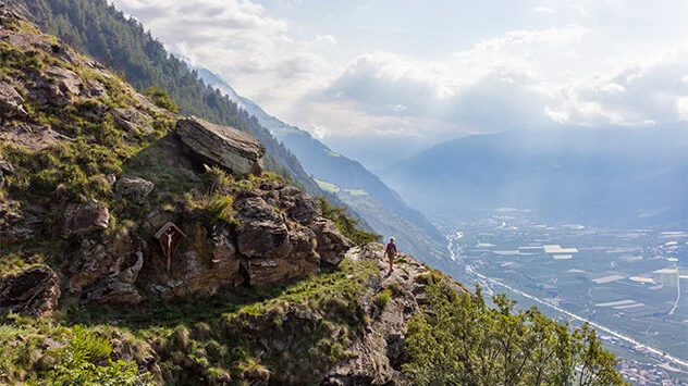 Frau wandert auf einem steilen Hang mit Aussicht auf die Berge