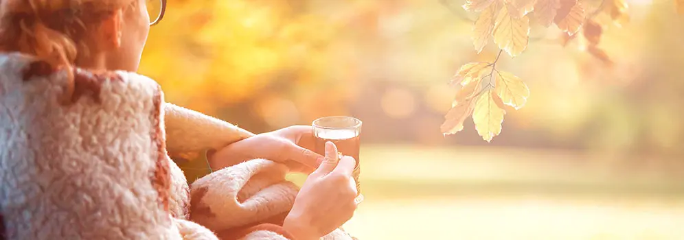 Frau sitzt mit Getränk draußen in der Herbstsonne
