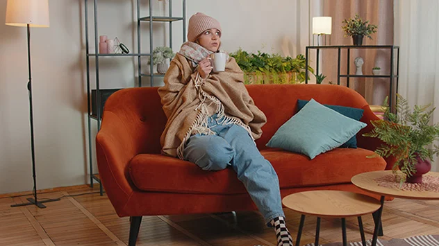 Frau sitzt mit warmer Kleidung auf Sofa