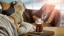 Ein Person liegt mit Socken und heißem Tee auf dem Sofa 