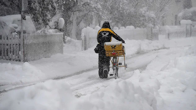 Postzusteller mit dem Fahrrad im Schneetreiben