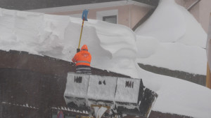 Mann schaufelt Schnee vom Dach