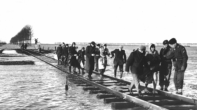 © dpa Bewohner des niederländischen Überschwemmungsgebietes in Zeeland bringen sich am 2.2.1953 über einen Schienenstrang in Sicherheit.