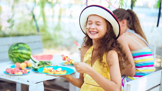 Junges Mädchen isst Obst im Garten und Wespe fliegt vor ihrem Gesicht