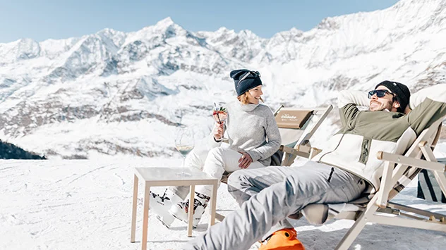 Ein Paar sonnt sich in Liegestühlen, im Hintergrund Berge.