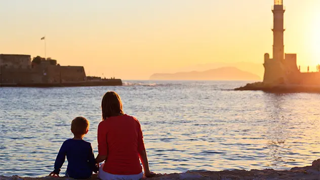Mutter sitzt mit Sohn am Hafen und schaut dem Sonnenuntergang zu