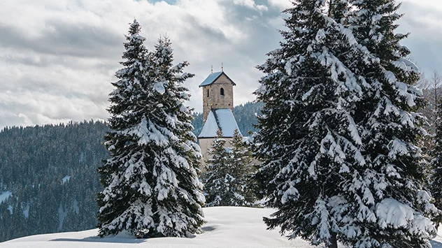 Die St.-Vigilius-Kirche in einer verschneiten Winterlandschaft. 
