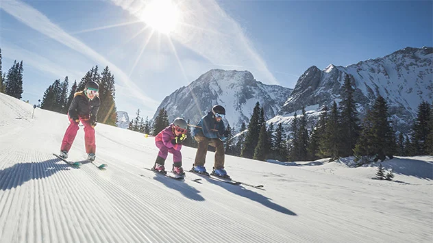 Eine Familie fahrt bei Sonnenschein eine Skipiste hinunter