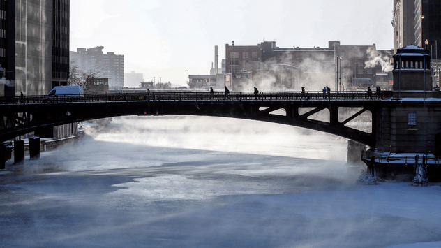 Varias personas cruzan un puente mientras la niebla se eleva desde el congelado río Chicago.