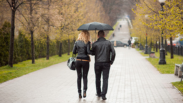 Paar mit Regenschirm in einem Park bei Regen unterwegs