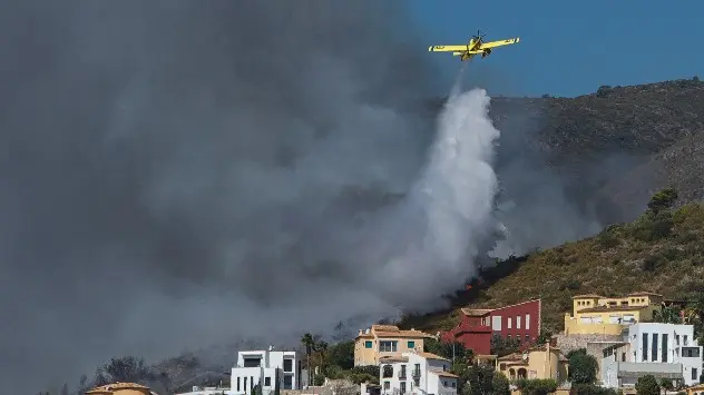 Ein Löschflugzeug verteilt Wasser auf die Flammen neben mehreren Häusern in der Gegend von Alicante in Spanien.