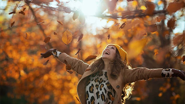 Frau wirft in der Herbstsonne Laub in die Luft