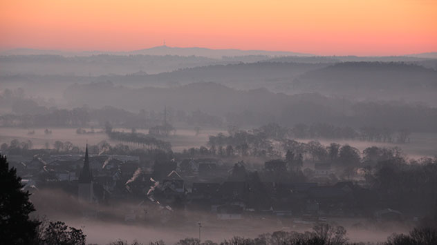 In Battenberg an der Eder in Hessen glüht der Himmel in orange Tönen, während grauer Nebel die Täler füllt. 