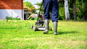 Ein Mann in Gummistiefeln mäht den Rasen