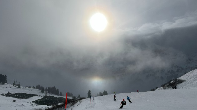 Skifahrer wedeln der Sonne entgegen. Dabei ist auch eine Untersonne zu erkennen. 