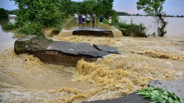 Flood-affected people stand on a road damaged by the flood waters after heavy rains in Nagaon district