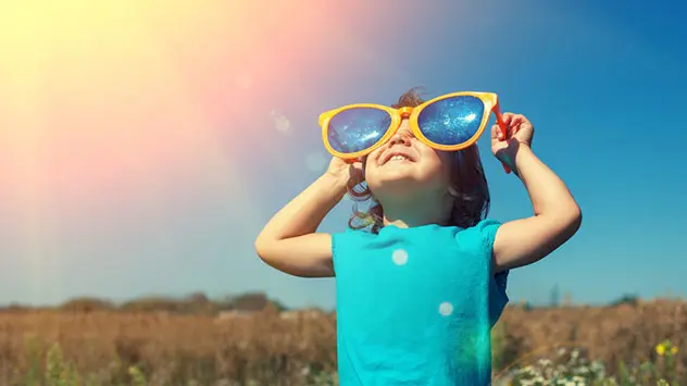 Kind schaut mit riesiger Sonnenbrille in den Himmel
