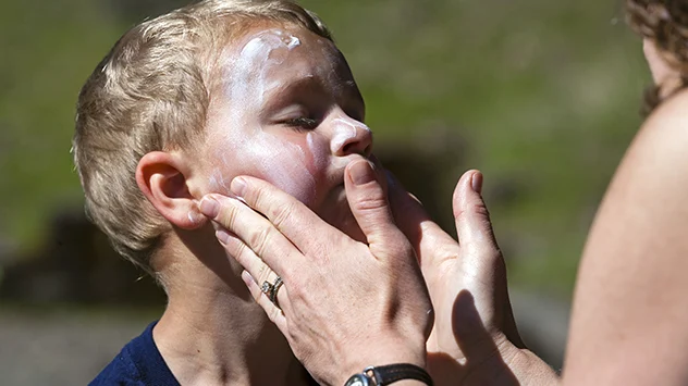 Eine Frau trägt einem kleinen Jungen Sonnencreme aufs Gesicht auf.