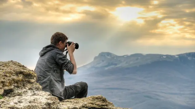 Man sits on rocky mountain with camera