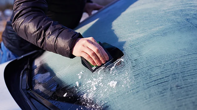 Eine Person kratzt Eis von einem Auto