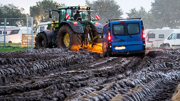 Ein Fahrzeug wird mit Hilfe eines Traktors auf das Gelände des Heavy-Metal-Festivals durch den Schlamm gezogen.