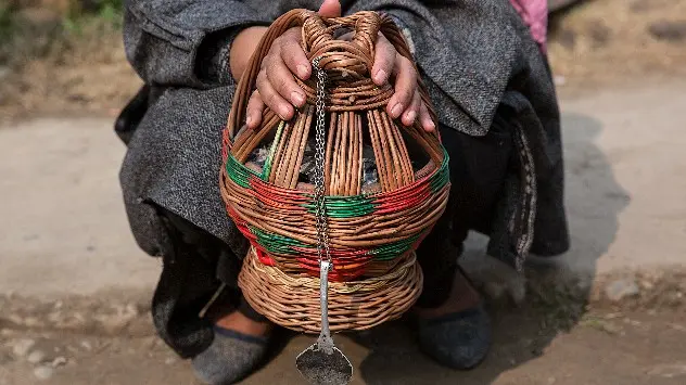 A woman in Kashmir warms her hands on a Kangri, a type of traditional fire-pots
