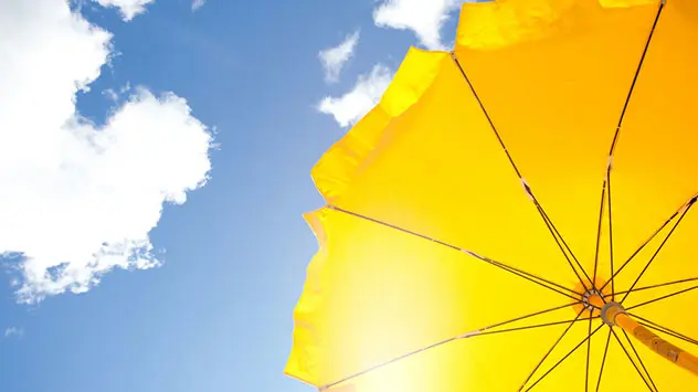 TIpps gegen Sonnenbrand: Schatten Gelber Sonnenschirm vor blauem Himmel hält die Sonne ab