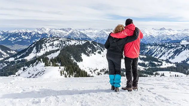 Paar blickt auf die verschneiten Berggipfel im Allgäu