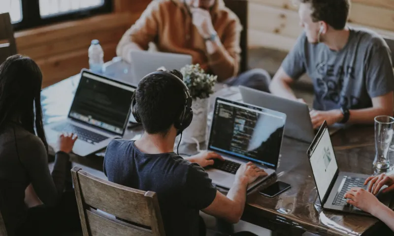 Engineers working at a table together with their laptops out.