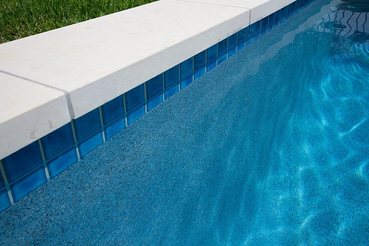 Blue pool tile beneath pale stone coping