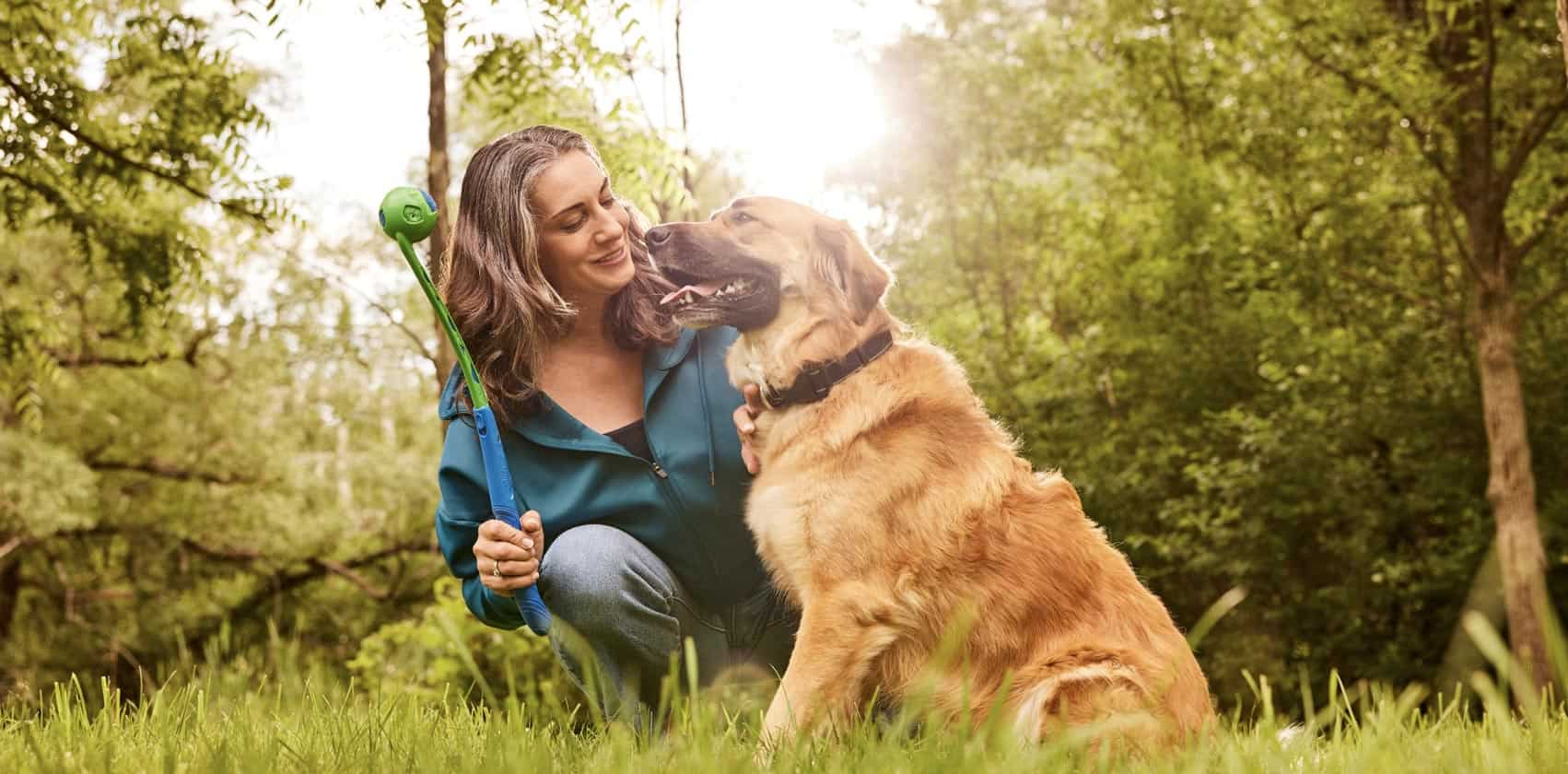 A woman and her tan and black dog play catch with a ball outdoors