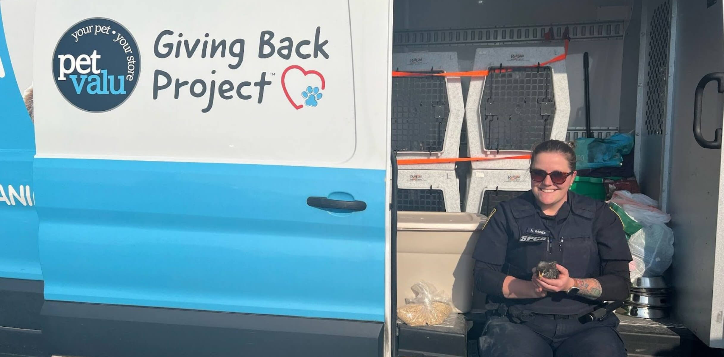 Smiling woman sits with a small chick in a van filled with pet supplies