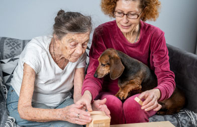 Daughter and older mother play a game on the couch with the family dog