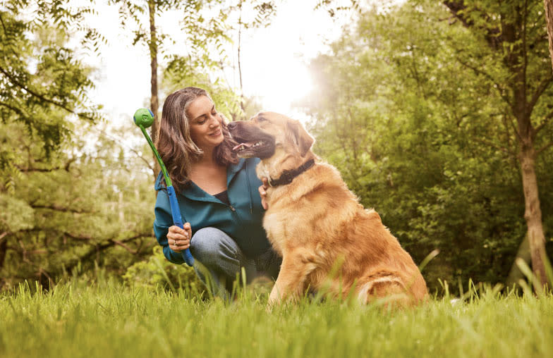 A woman and her tan and black dog play catch with a ball outdoors