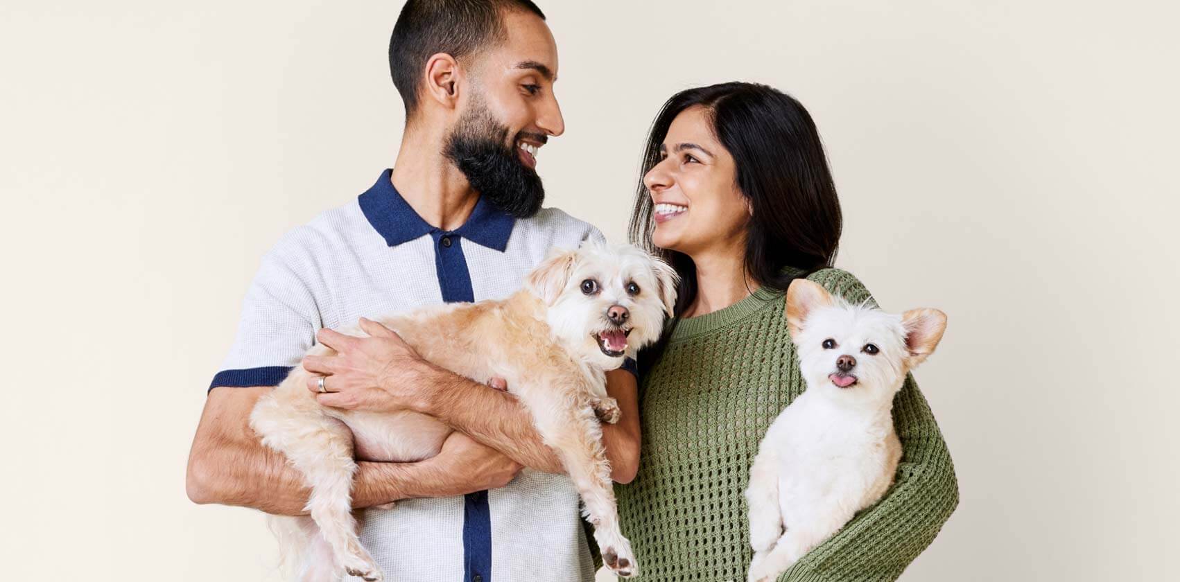  young man and woman hold a friendly, medium tan dog and a small white dog and pose for a photo