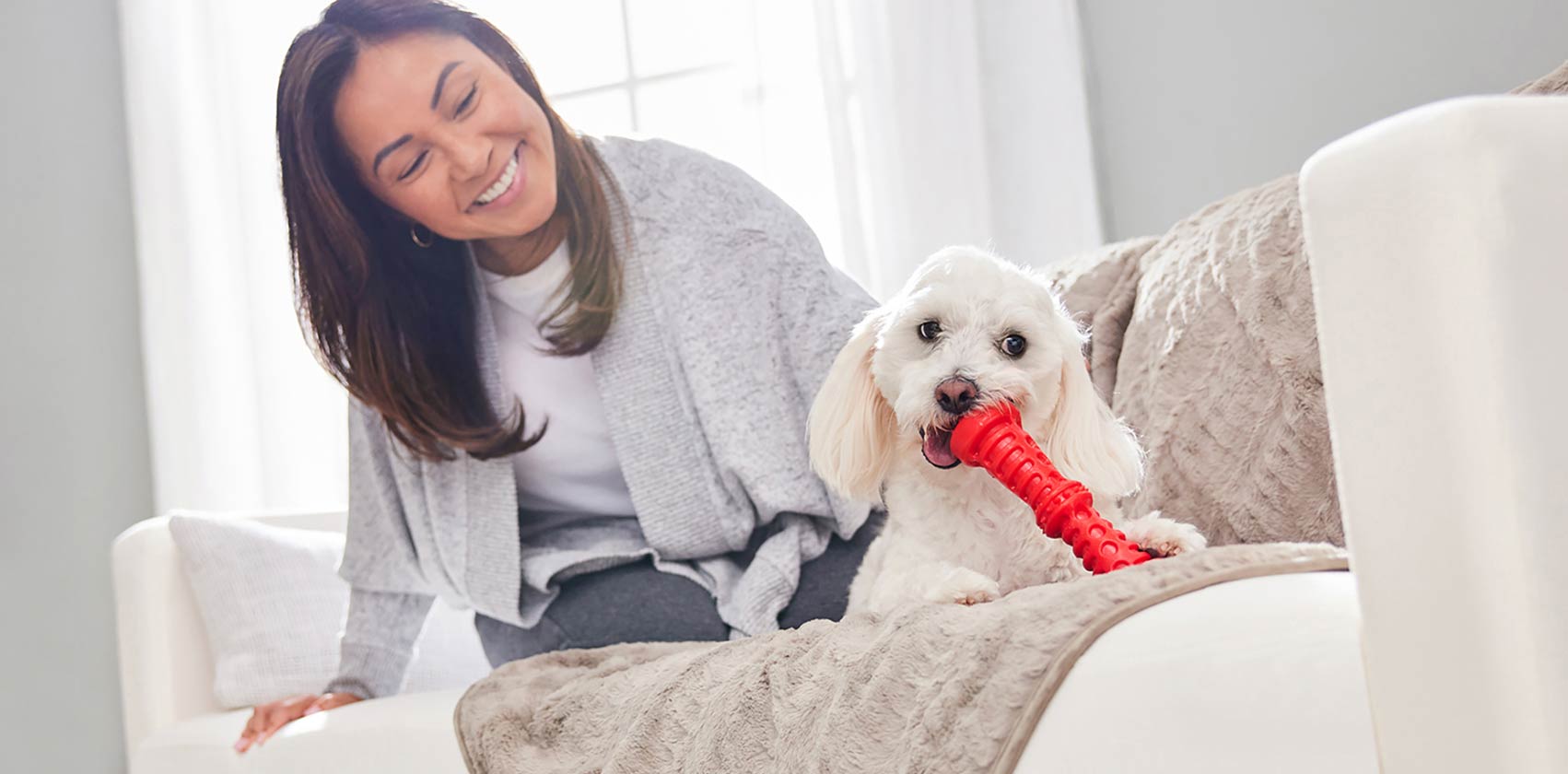 A white dog plays with a red toy next to their smiling DPL